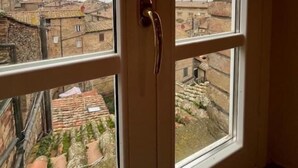 A room with a view of a traditional village through a window with a wooden door. - Suite dei Cherubini (Volterra)