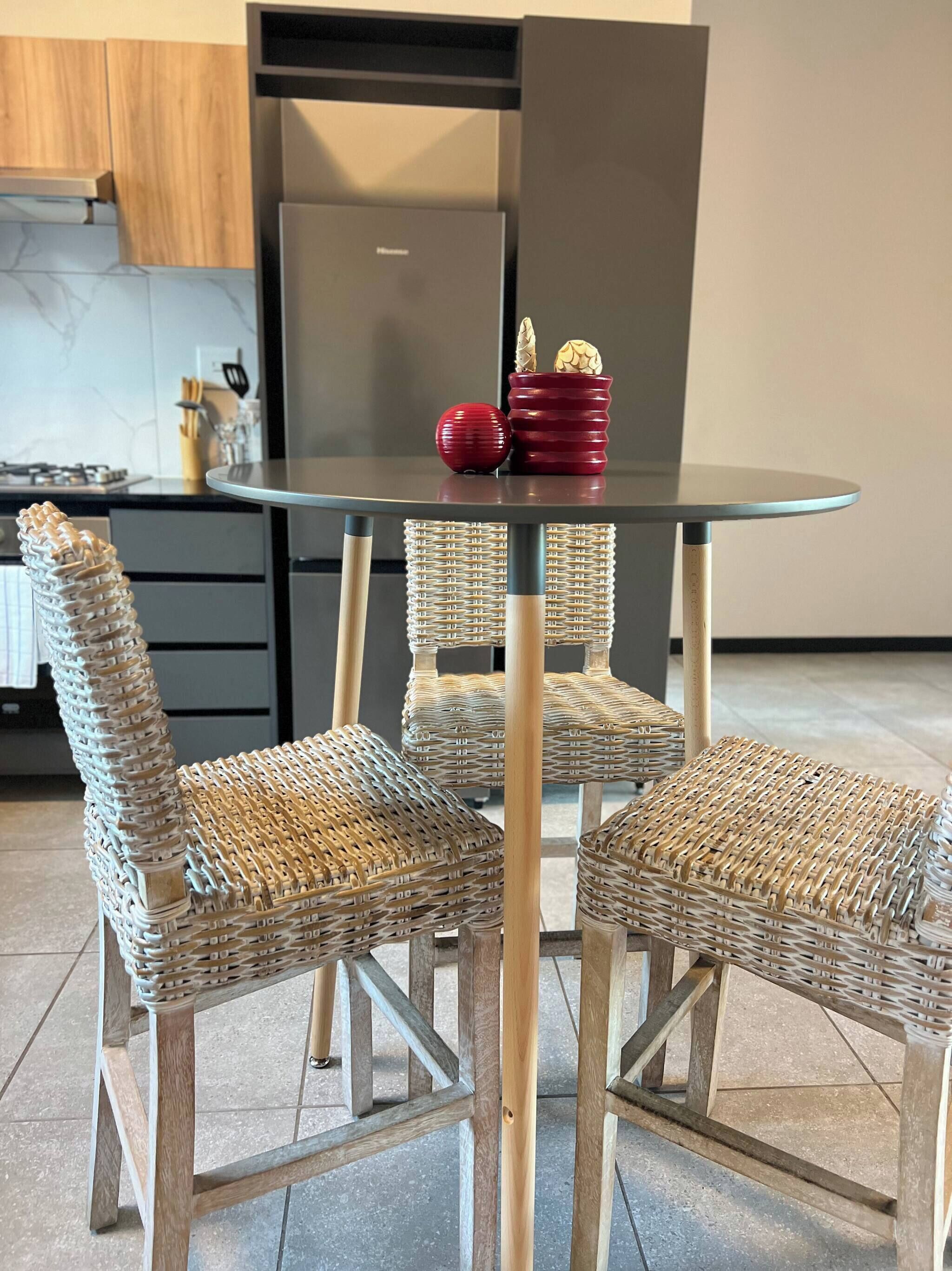Et moderne køkken med fletstole, et glasbord og en rød vase med dekorative genstande.