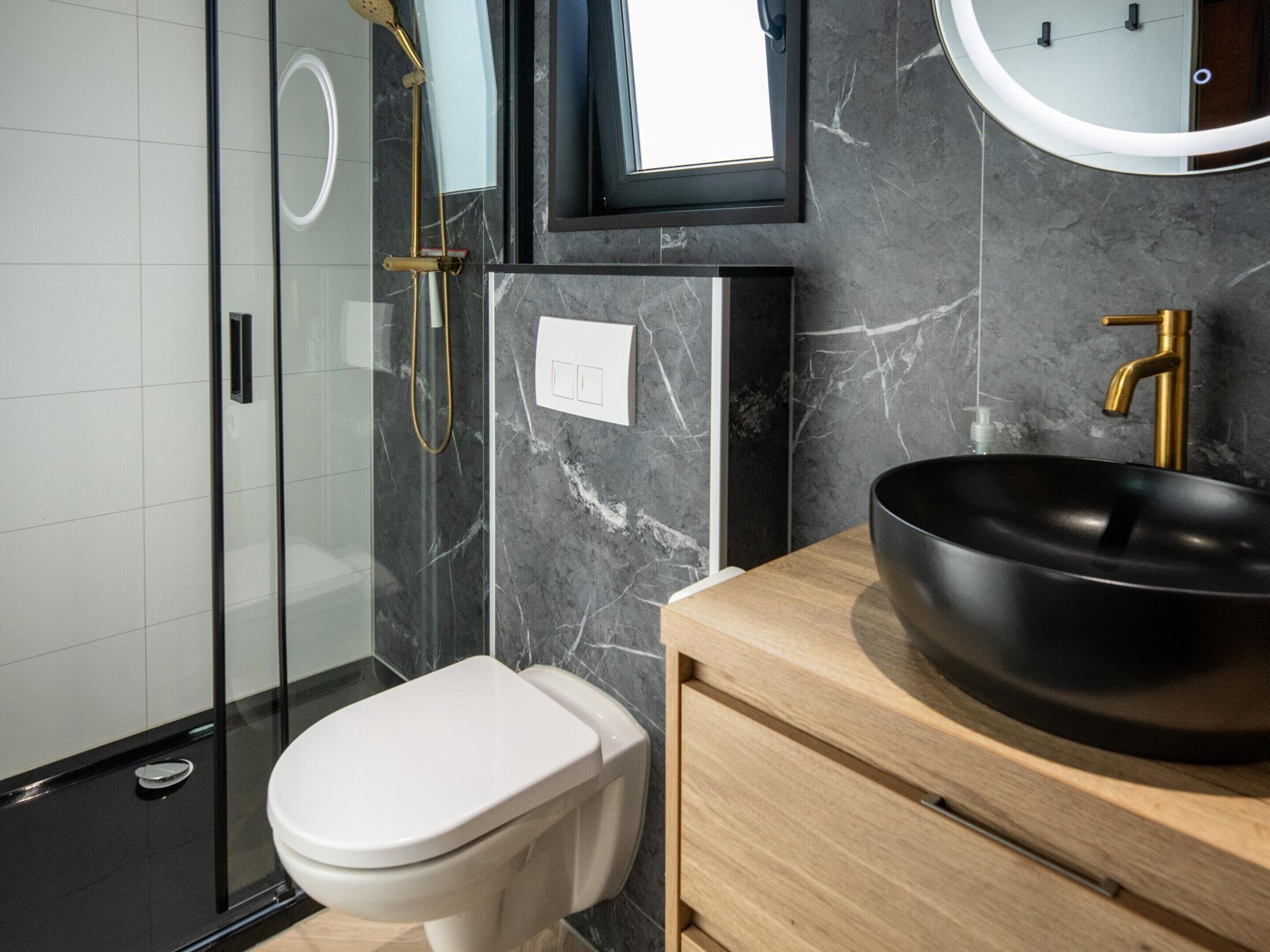 A modern bathroom with a toilet, a black sink, and a glass shower enclosure.