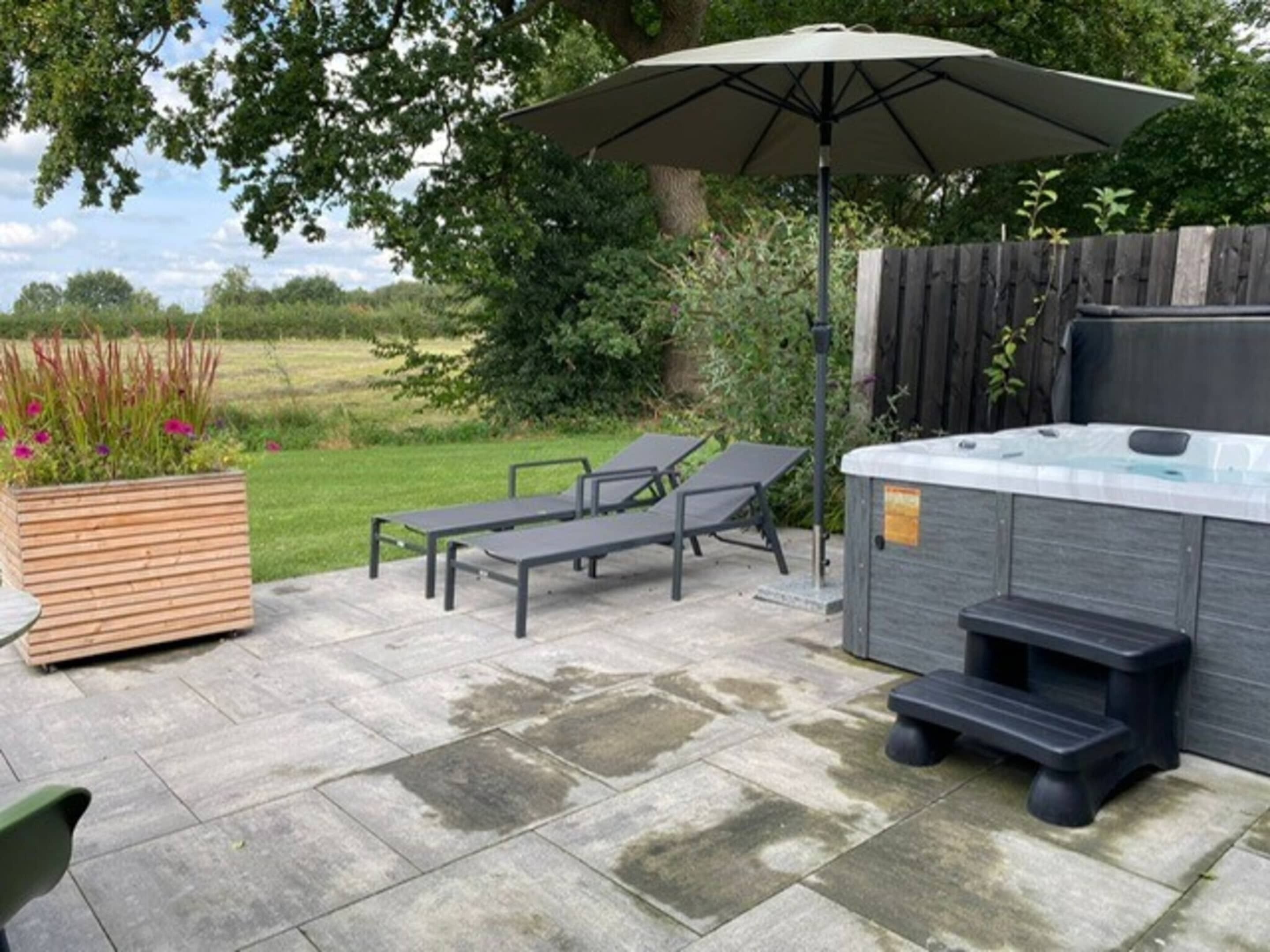 Une terrasse extérieure dotée d’un jacuzzi, de chaises longues et d’un jardinier en bois rempli de fleurs.