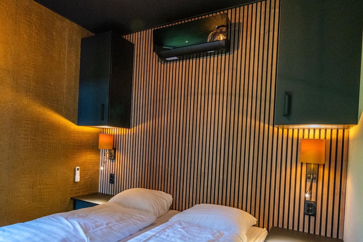 Ein Hotelzimmer mit einem Bett, zwei Nachttischlampen, einem an der Wand befestigten Fernseher und einer Holzvertäfelung.