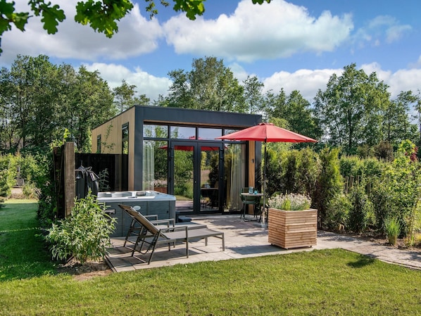 A modern outdoor hot tub area with a glass enclosure, a wooden deck, and a red umbrella.