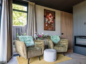 A modern living room with two armchairs, a round ottoman, a painting, and a wooden panel wall. - Private Sauna at Wellness Lodge in Drenthe (Dalerveen)