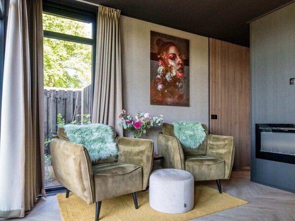 Ein modernes Wohnzimmer mit zwei Sesseln, einem runden Hocker, einem Gemälde und einer Wandpaneele aus Holz.