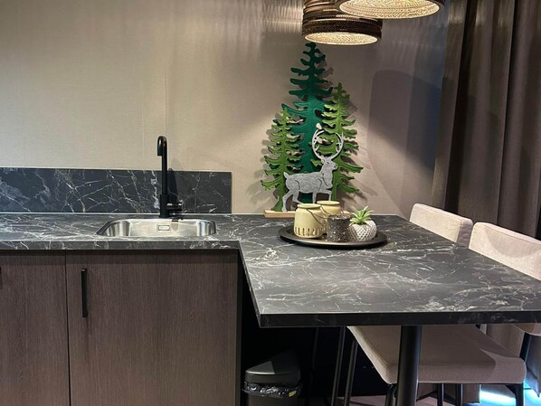 Une cuisine moderne avec un plan de travail en marbre, un robinet noir, un arbre décoratif orné d’un cerf et une petite plante en pot.