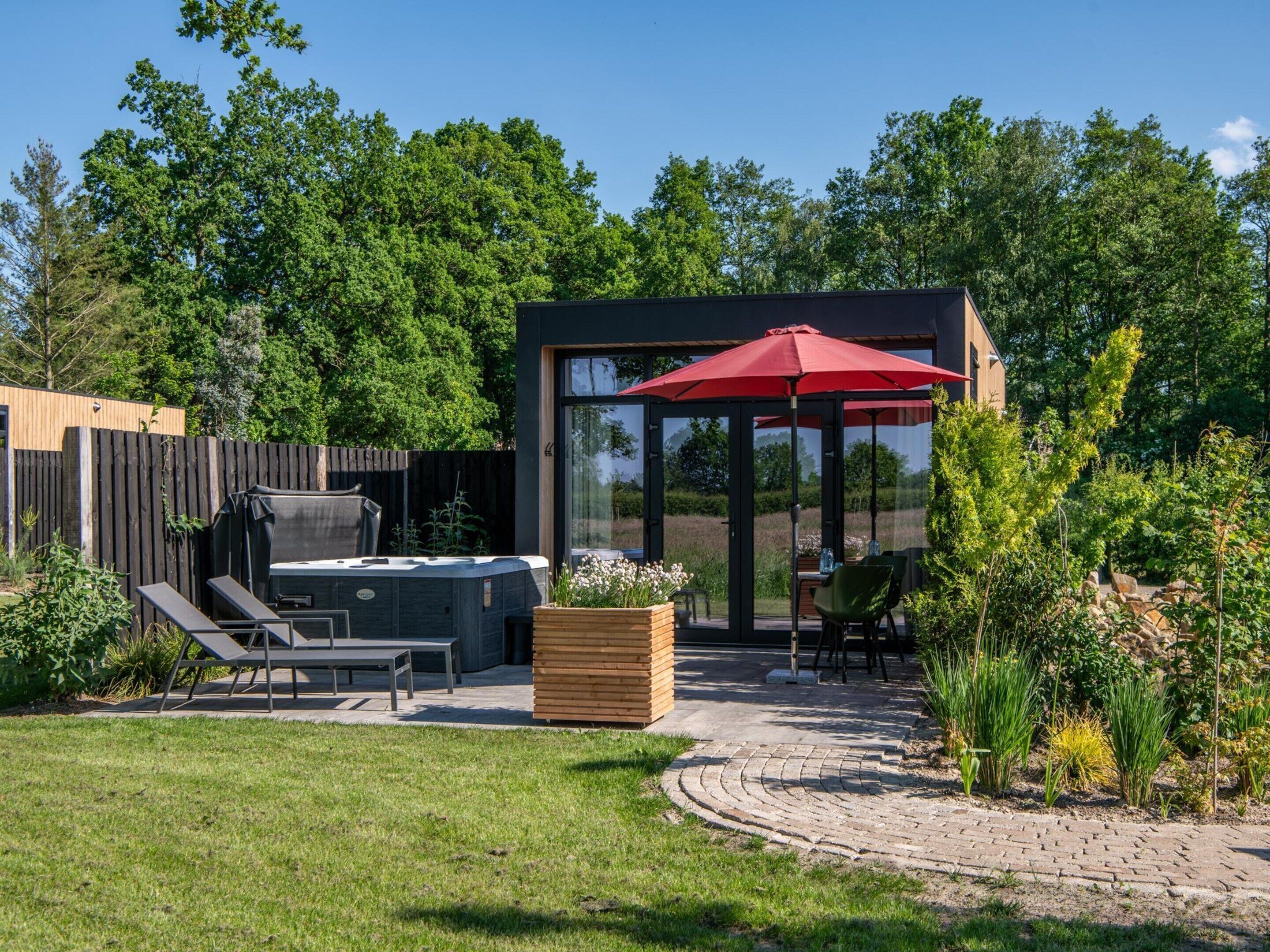 A modern outdoor patio with a hot tub, seating, and a glass-enclosed structure.