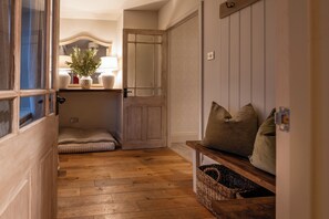 A hallway with wooden flooring, a bench with cushions, a door, and a wall-mounted shelf with a plant. - Riverwalk Cottage - A Charming Newly Renovated Stone Cottage (Warkworth)
