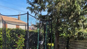 A trampoline, a slide, and a fenced area with trees and a building in the background. - Family home (Semussac)