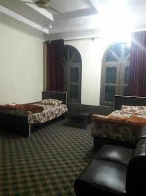 Una habitación con dos camas, un sofá, una mesita y una ventana con cortinas.