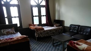Habitación con dos camas, un sofá, una mesa y ventanas amplias con cortinas.