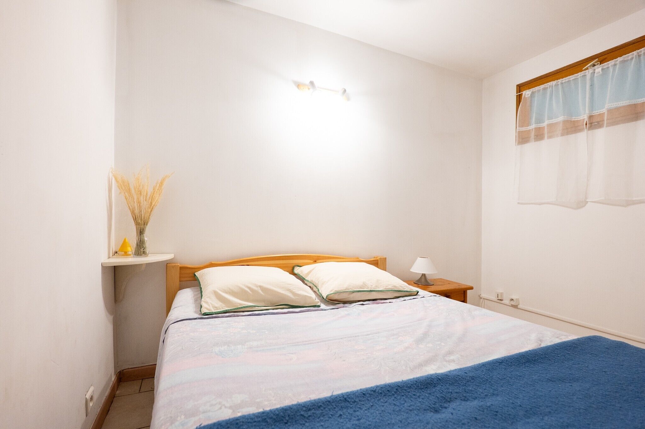 Un dormitorio con cama, mesita de noche, lámpara y aplique en la pared.