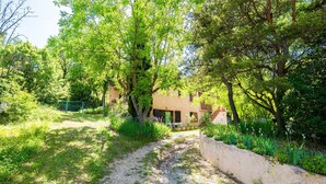 Un chemin de gravier mène à un bâtiment entouré d’une végétation luxuriante et d’arbres.