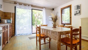 Un espace repas comprenant une table, des chaises, une cuisine équipée et une vue à travers une porte vitrée.