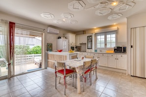 A kitchen with white cabinets, a dining table with chairs, and a sliding glass door leading to an outdoor area. - Family Home Near the Beach (Le Grau-du-Roi)