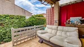 Eine überdachte Terrasse mit einem weißen Tor, einem beigefarbenen Sofa, einem roten Vorhang und einer Holzkabine mit verschiedenen Gegenständen.