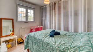 Ein Schlafzimmer mit einem Bett, einem Babybett, einem Fenster und einem Schreibtisch mit Spiegel und Spielzeug.