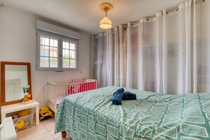 Een slaapkamer met een bed, een ledikant, een raam en een bureau met een spiegel en een speeltje.