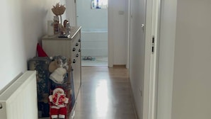Kapea käytävä, jossa on puulattia, vasemmalla puolella patteri, pieni pöytä, jonka päällä on joulupukki-koriste, ja käytävän päässä ovi.