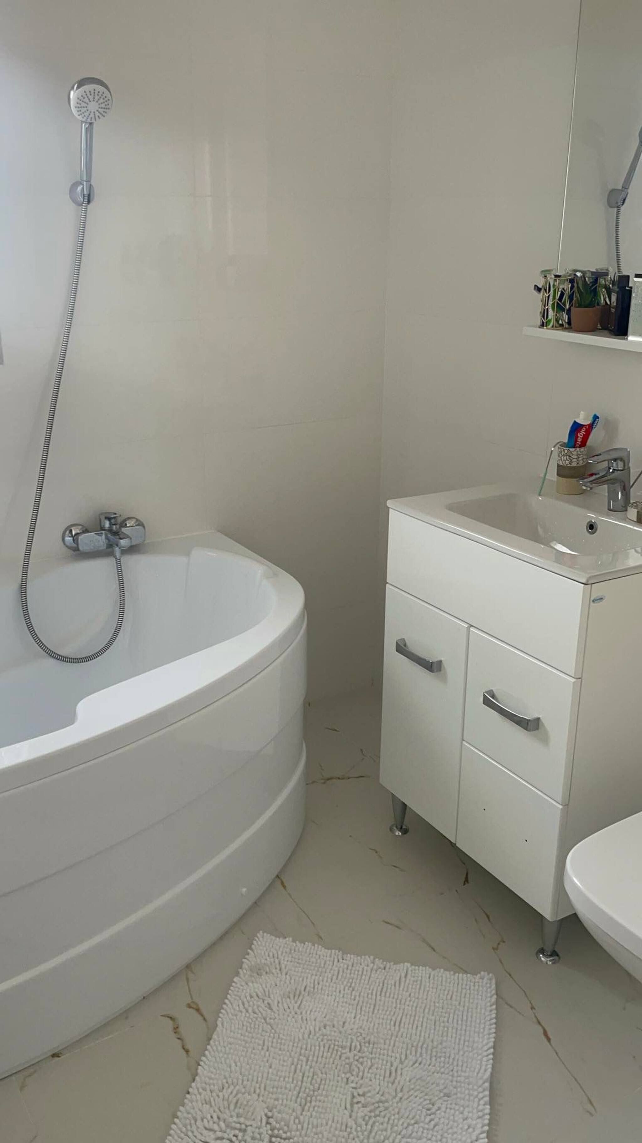 Un baño con una bañera independiente, un tocador blanco con cajones, un lavabo y un cabezal de ducha.