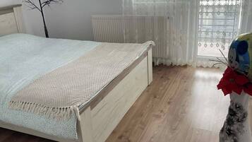 Un dormitorio con una cama de madera, un radiador y una ventana con cortinas estampadas.