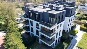 Ein mehrstöckiges Gebäude mit Balkonen, einer flachen Dachterrasse und einem Garten.