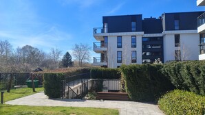 Ein modernes Mehrfamilienhaus mit geschlossenem Eingangsbereich, einer Treppe und einem gepflegten Garten.