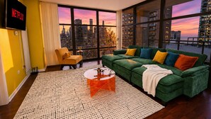 A modern living room with a green sofa, a yellow armchair, a coffee table, and a large window with a city view.