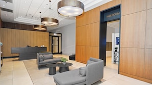 A modern lobby with a reception desk, grey sofas, a coffee table, and a mailroom entrance.