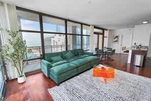 Ein modernes Wohnzimmer mit einem grünen Sofa, einem Essbereich und Blick auf die Stadtlandschaft.