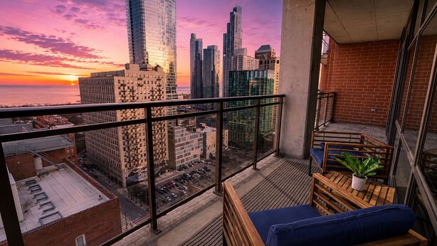 A balcony with a view of a cityscape at sunset, featuring high-rise buildings and a clear sky.