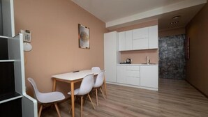 A modern kitchen with white cabinets and a dining area with a table and chairs. - Hotel Gloria KS (Pristina)