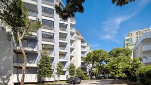 Un immeuble résidentiel à plusieurs étages, doté de balcons, d’un espace de stationnement et d’arbres.