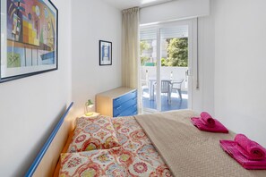 Une chambre à coucher avec un lit, un bureau, une chaise, une fenêtre et un balcon.