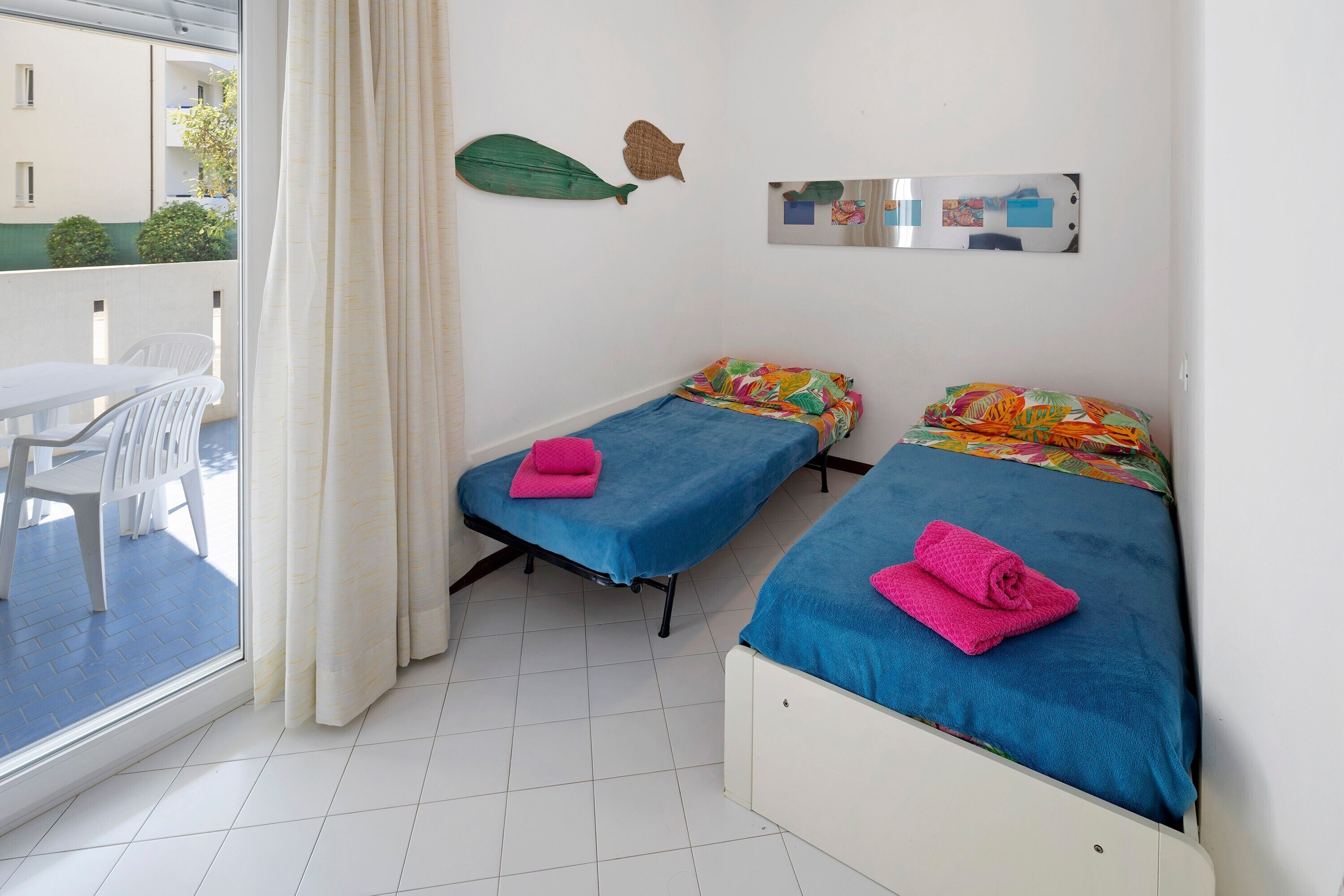 A room with two beds, a table, chairs, and a view of the outside.