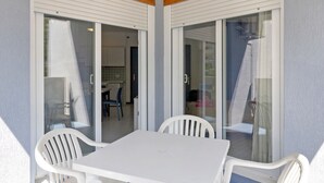 Ett takförsett utomhusområde med ett bord och stolar, skjutbara glasdörrar som leder in till ett inomhusutrymme och ett träpanelat tak.