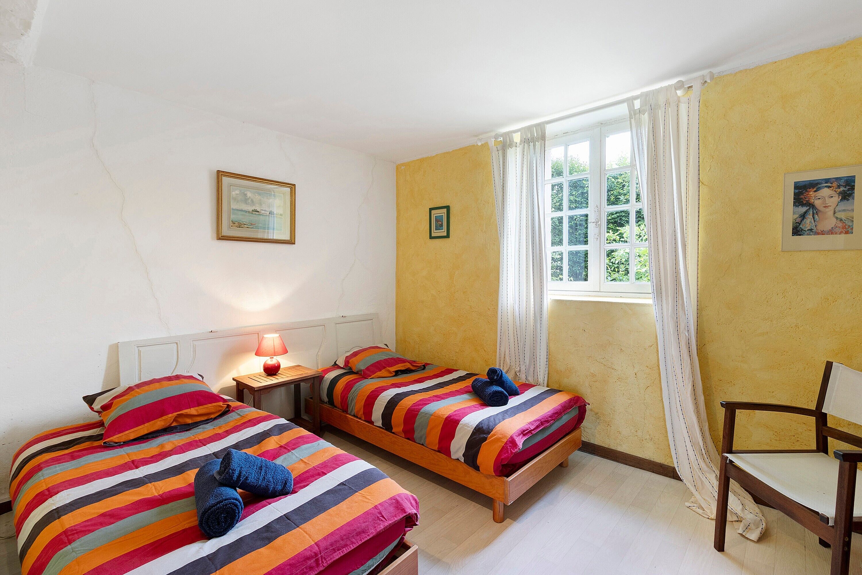 Une chambre avec deux lits, une chaise, une fenêtre avec des rideaux et une lampe.