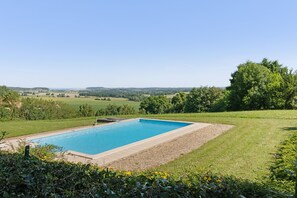 A rectangular swimming pool with a clear blue water surface, surrounded by a gravel area and a grassy lawn.