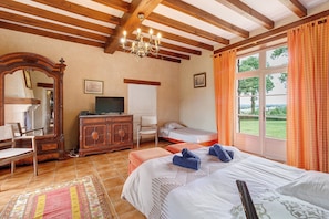 Ein Schlafzimmer mit Bett, Kommode, Fernseher, Fenster mit Vorhängen und einer Deckenleuchte.
