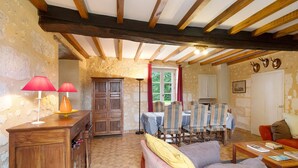 A rustic room with exposed wooden beams, a dining area with striped chairs, a sofa, and a wooden cabinet with a lamp.