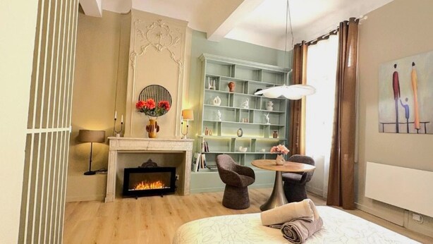 Una habitación de hotel con chimenea, una mesa redonda con sillas, una estantería y un cuadro en la pared.