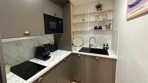 Una cocina compacta con microondas integrado, un lavamanos y una encimera con cafetera.