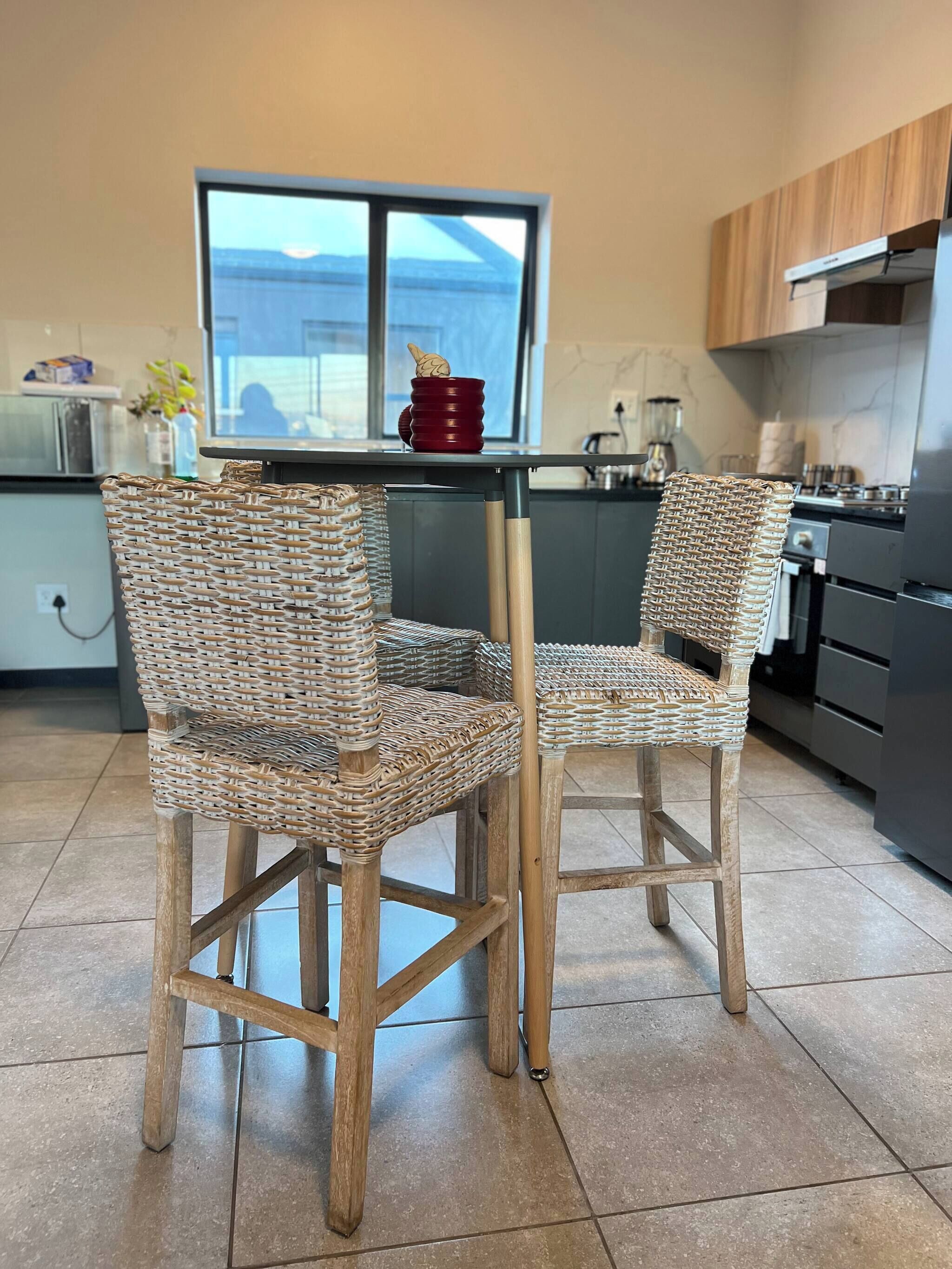 A kitchen with two wicker chairs, a red bowl, and a window with a view.