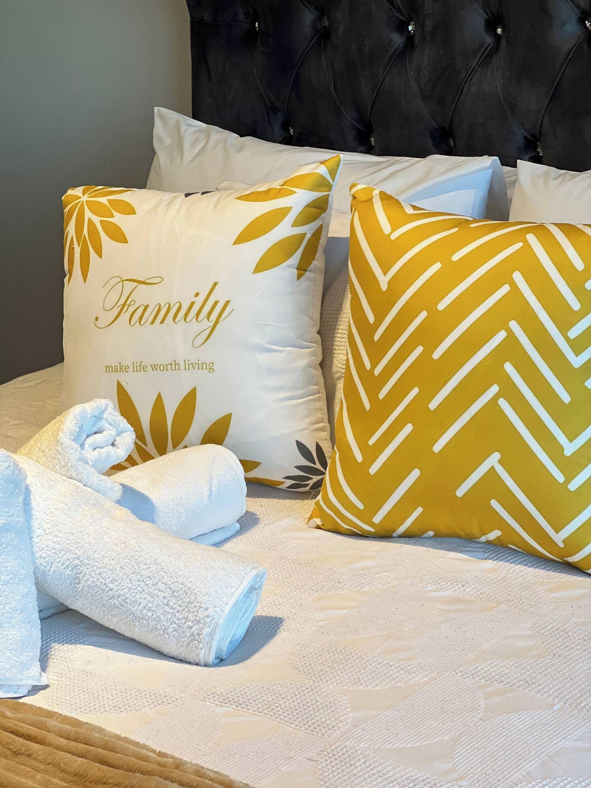 A bed with two decorative pillows, a rolled white towel, and a headboard.