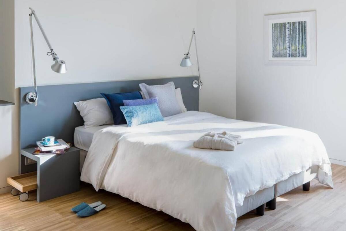 A neatly made bed with white bedding, a small bedside table with a lamp, and a framed picture on the wall.