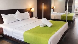 Habitación de hotel con una cama grande, una mesita de noche, un espejo y un detalle verde en la colcha.