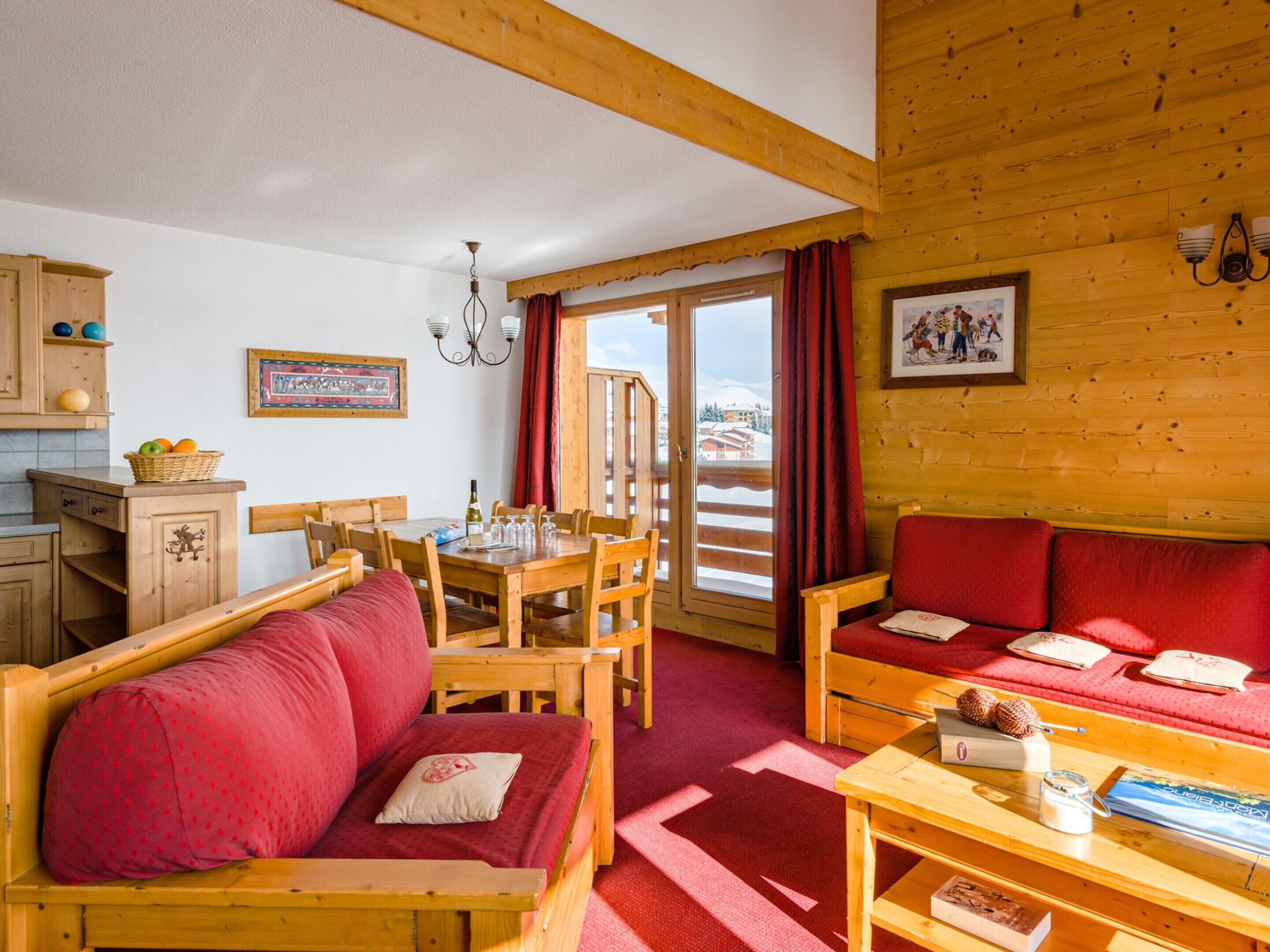 A cozy log cabin interior with a dining area, wooden furniture, and a view of the snowy landscape.