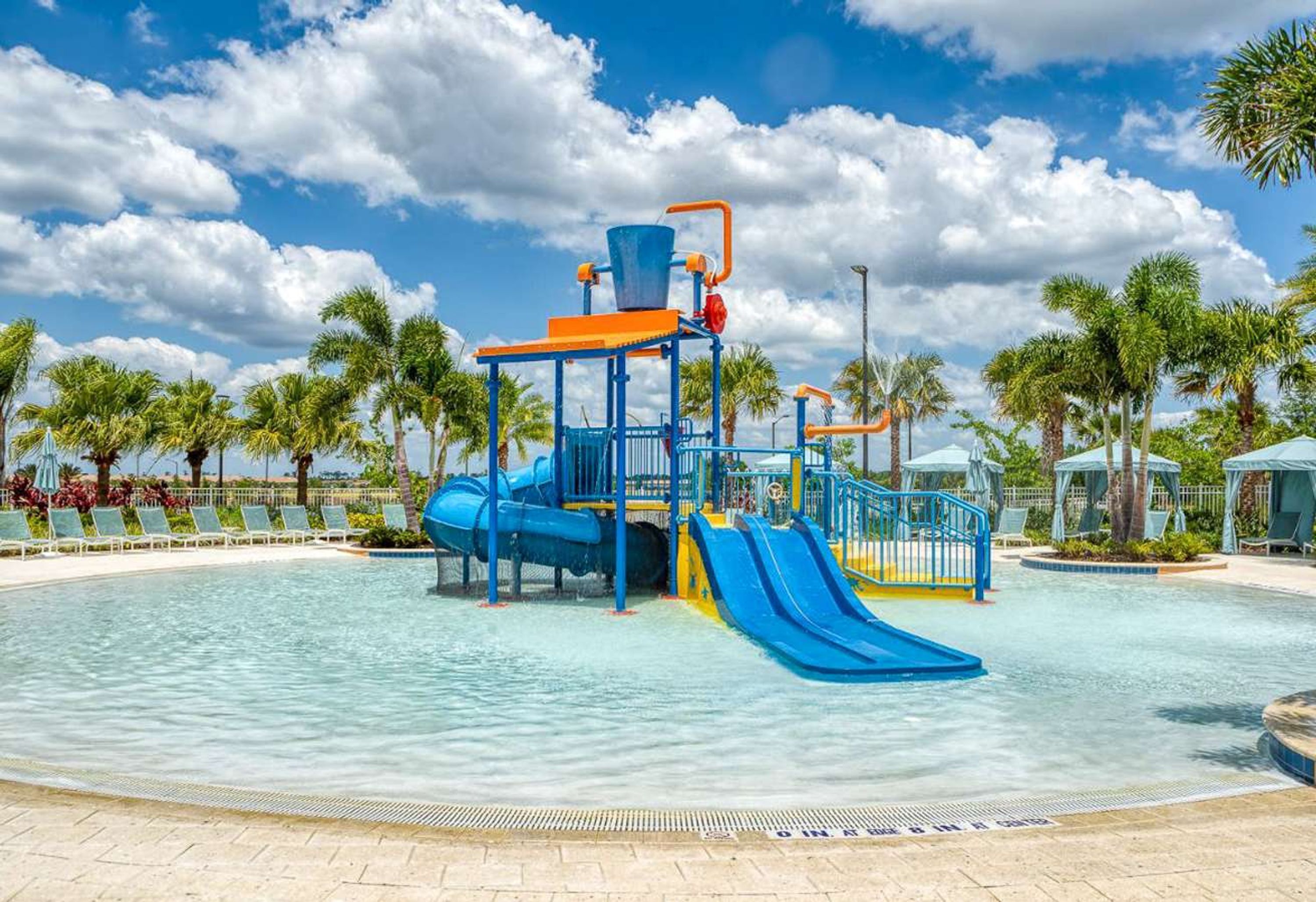 Parque acuático con una estructura de juego azul y naranja, palmeras y cielo despejado.