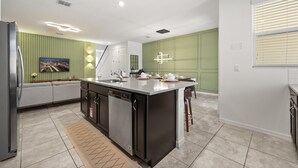 A modern kitchen with a central island, built-in dishwasher, and a green accent wall. - Upstay Modern Home Near Disney With Pool (Kissimmee)