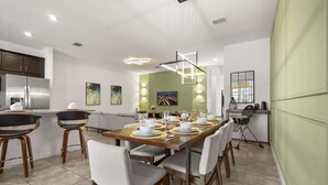 A modern kitchen with a dining area, featuring a large island, bar stools, and a dining table set for six. - Upstay Modern Home Near Disney With Pool (Kissimmee)