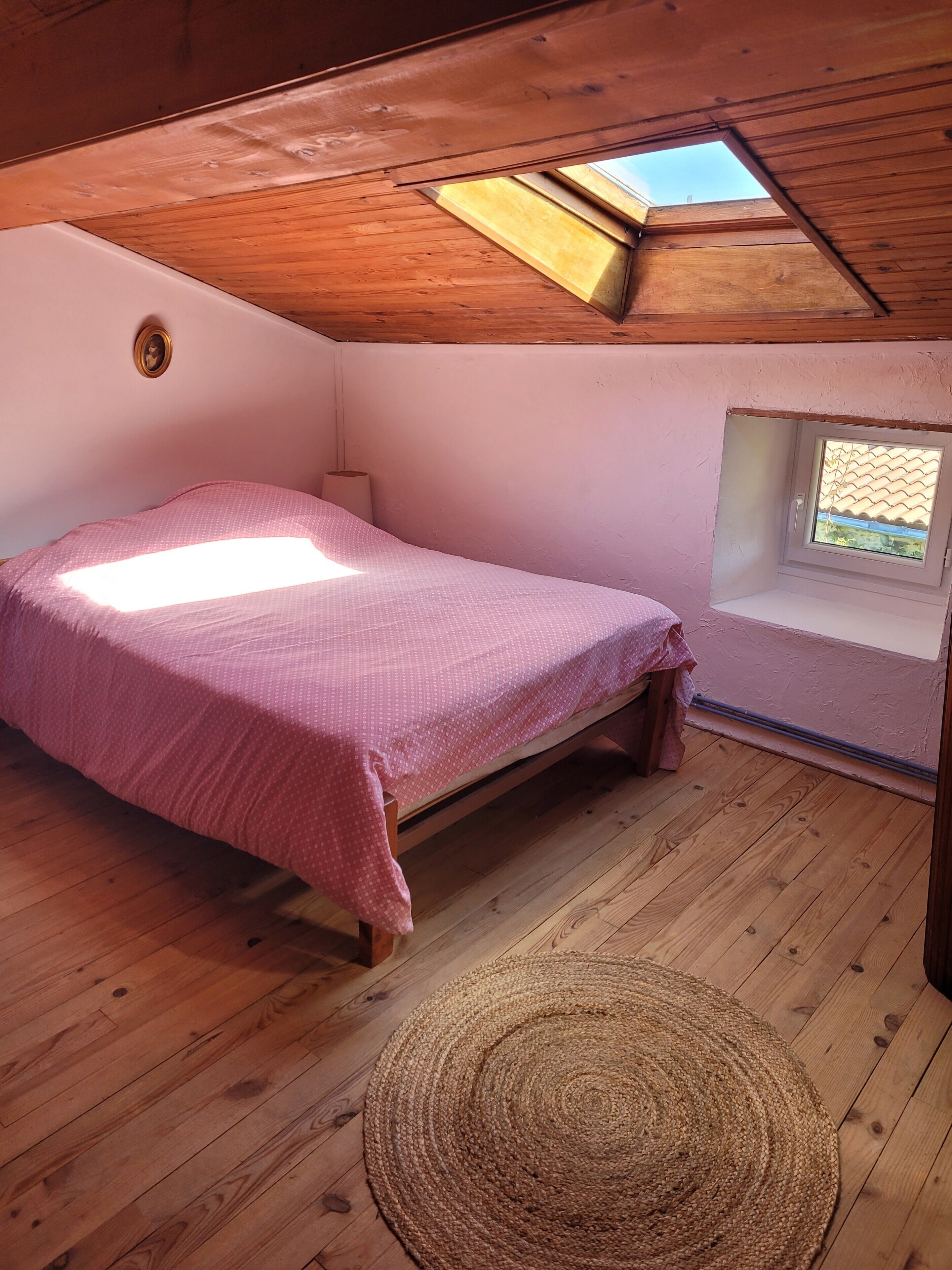 Una habitación pequeña y acogedora con techo inclinado, una cama individual, una ventana y un tragaluz.